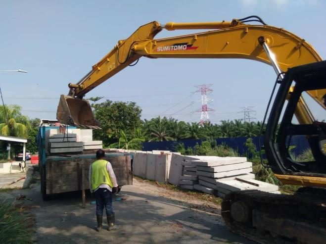 Excavator handling precast IBS fence panels with workers