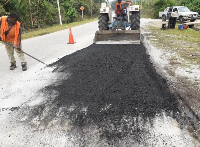 Worker raking asphalt by hand at a road edge