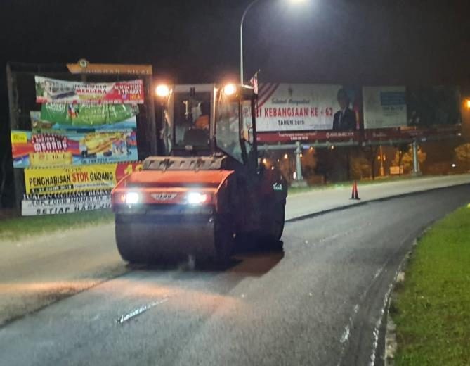 Road roller compacting fresh asphalt at night